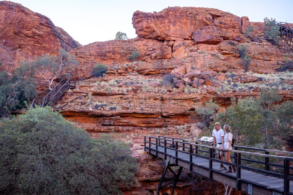 Feel on top of the world as you walk along the towering red rock cliffs of Kings Canyon and take in views of the forest of palms below.<br /><br />Watarrka National Park is only three hours?? drive from Uluru, and is home to the mighty Kings Canyon – a majestic destination featuring 300m high sandstone walls, palm-filled crevices, and views that stretch across the desert.